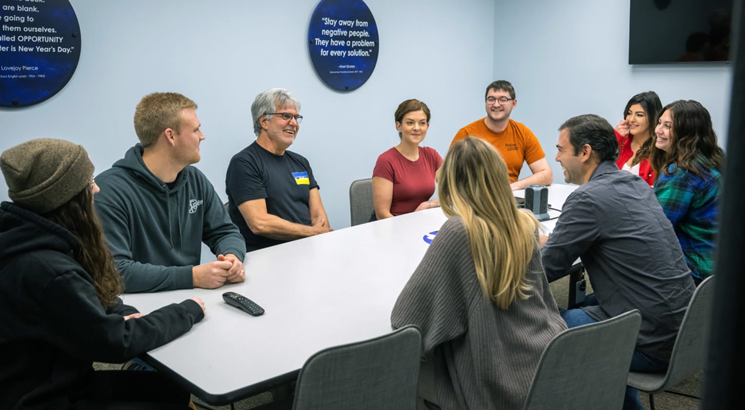 A diverse group of people engaged in discussion around a conference table in the Logistics Plus office.